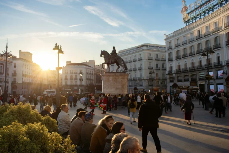 Tłumy ludzi na Plaza Puerta del Sol w Madrycie o zachodzie słońca, z widocznym pomnikiem króla Karola III