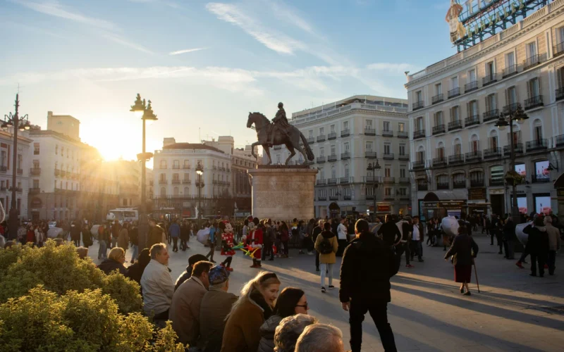 Tłumy ludzi na Plaza Puerta del Sol w Madrycie o zachodzie słońca, z widocznym pomnikiem króla Karola III