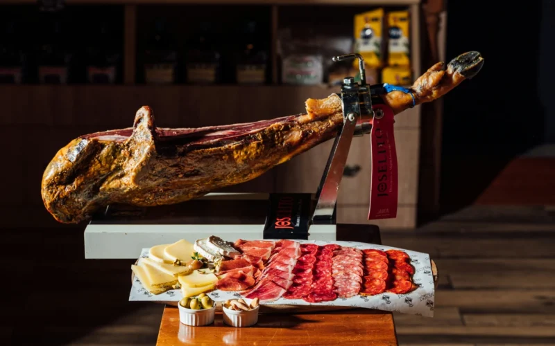 Jamón Ibérico serwowany na desce do krojenia z towarzyszącymi serami i oliwkami w tle